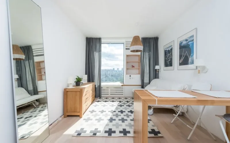 Wooden table and drawer placed in room with big window and wall decorated with pictures in light room with mirror