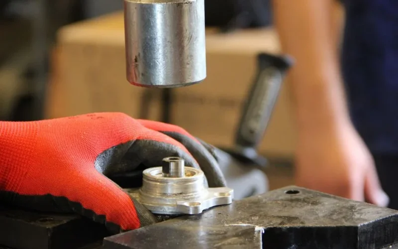Hands in red gloves operate metal machinery in workshop close-up.
