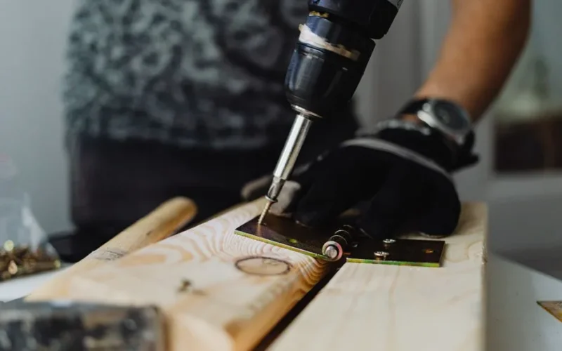 Focused close-up of a handyman using a drill on a wooden plank indoors.