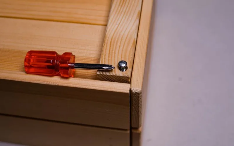 A screwdriver beside a screw on a wooden box, depicting carpentry work.