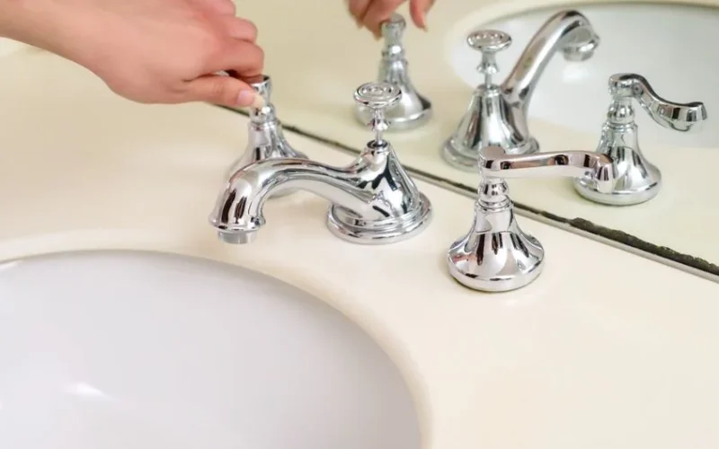 Close-up of a hand adjusting a chrome faucet in a modern bathroom interior.