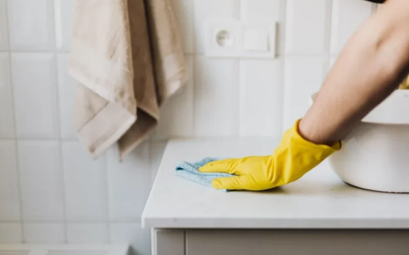 Crop anonymous woman in yellow protective gloves cleaning surface of cabinet near sink in bathroom during housework