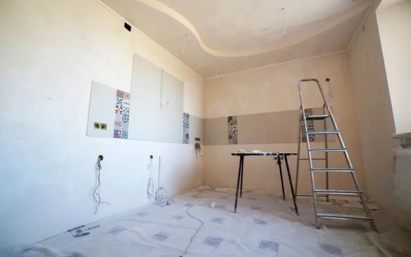 Interior view of a room under renovation with paint, tiles, and tools.