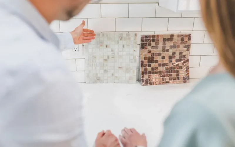 A couple examines decorative mosaic tiles for interior design in a contemporary kitchen setting.