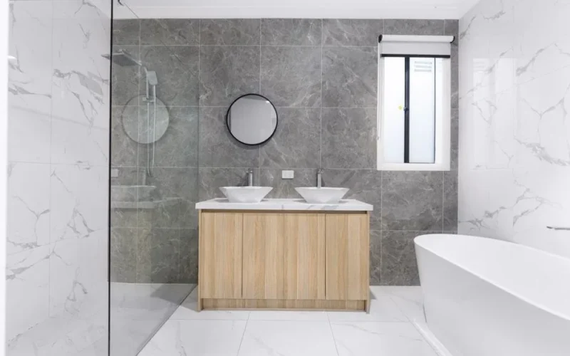 A sleek and stylish modern bathroom with minimalist design, featuring dual washbasins, marble tiles, and a glass shower enclosure.