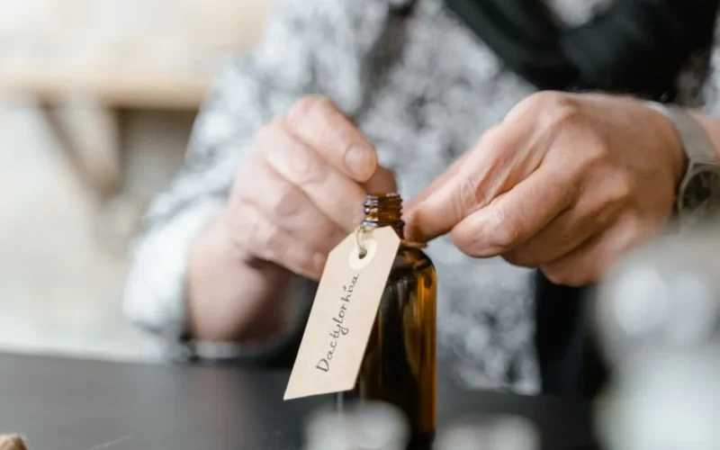 Close-up of a person attaching a label to a brown glass bottle indoors.