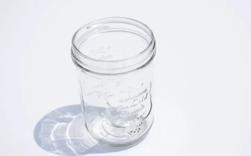 High-angle shot of an empty clear glass jar casting a shadow on a white surface.