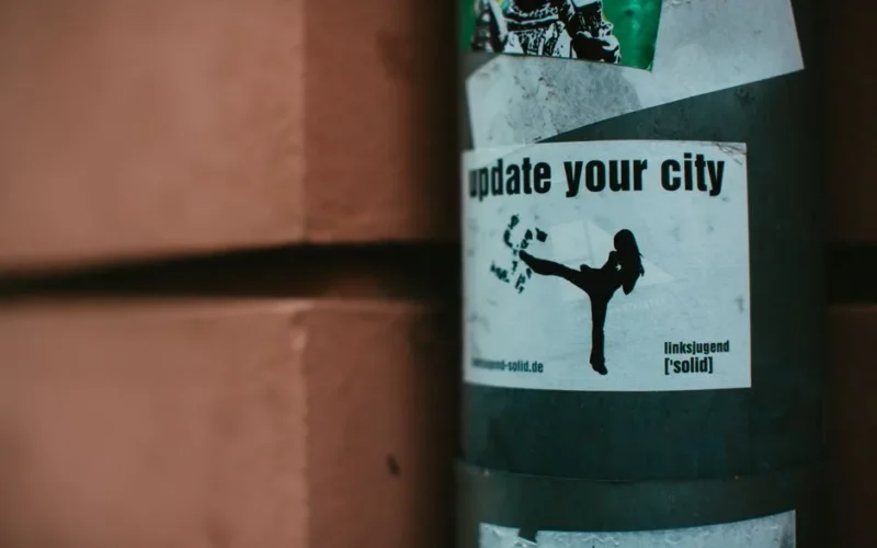 Close-up of urban stickers on a city street pole, highlighting street art and activist themes.