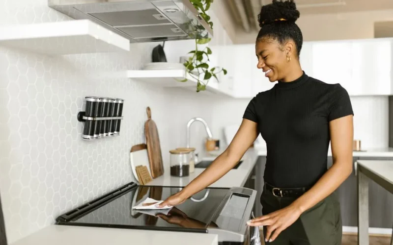 A woman is cleaning the kitchen stove top, showcasing modern housekeeping and responsibility.