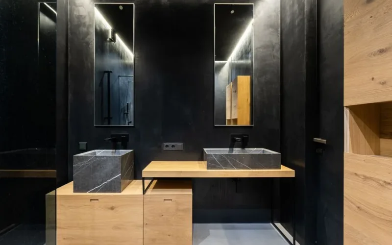 Washbasins with faucets placed on wooden table and cabinet near black wall with mirrors in modern washroom with door at home