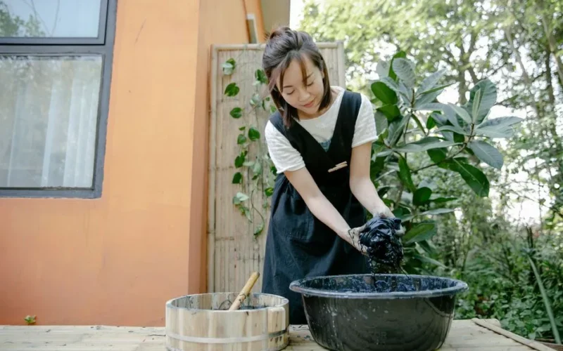 Woman engaged in fabric dyeing in a garden setting, mixing colors in bowls.
