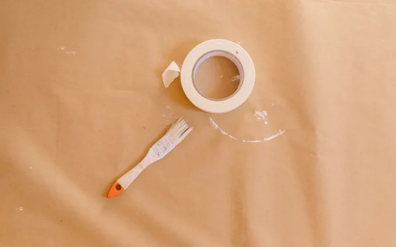 Close-up of a paintbrush and masking tape on a brown paper surface, ideal for DIY projects.