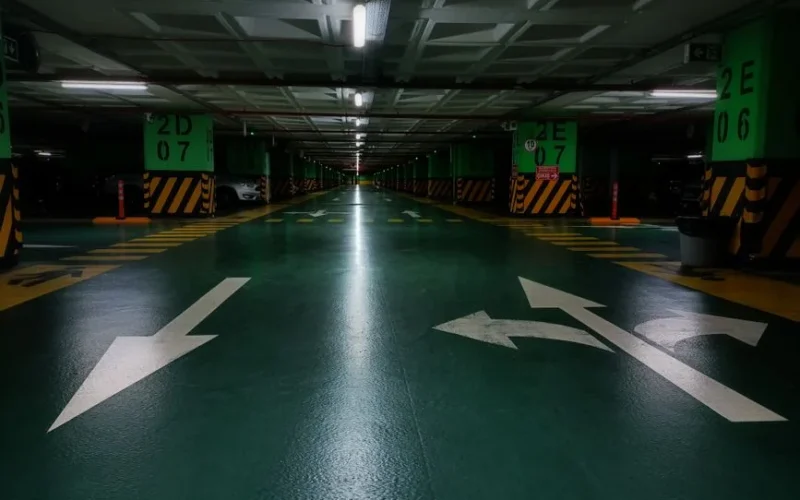 Dimly lit underground parking lot with directional arrows and green floor marking.