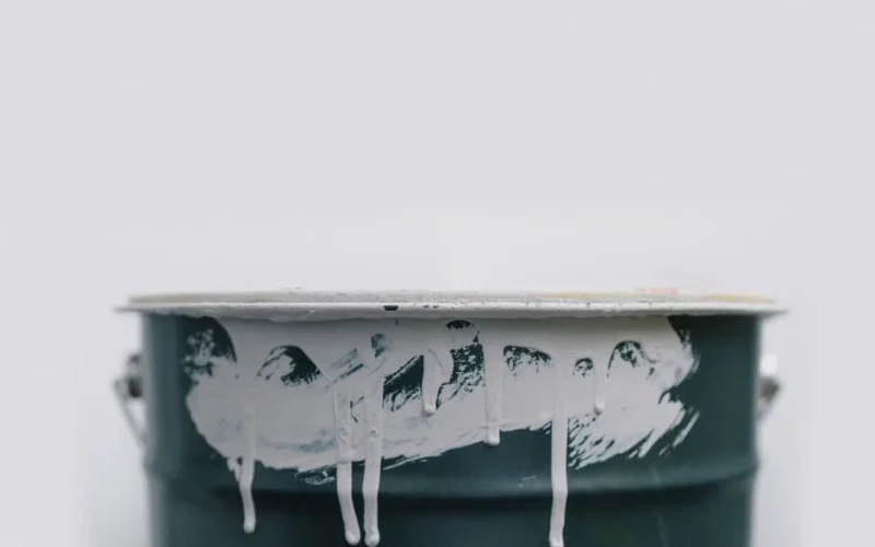 Closeup of white drips from paint on green metal bucket during repair at home