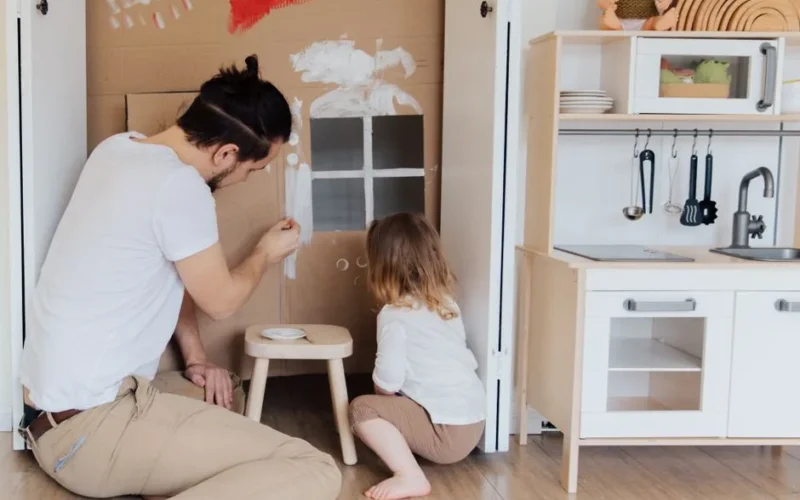 A father and child enjoying creative painting time indoors with a cardboard house.