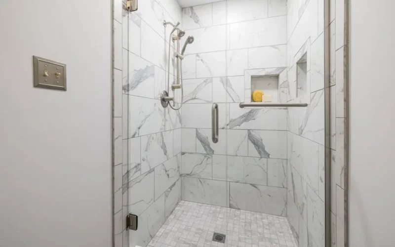 Elegant bathroom with white marble tiles and glass door, showcasing modern interior design.