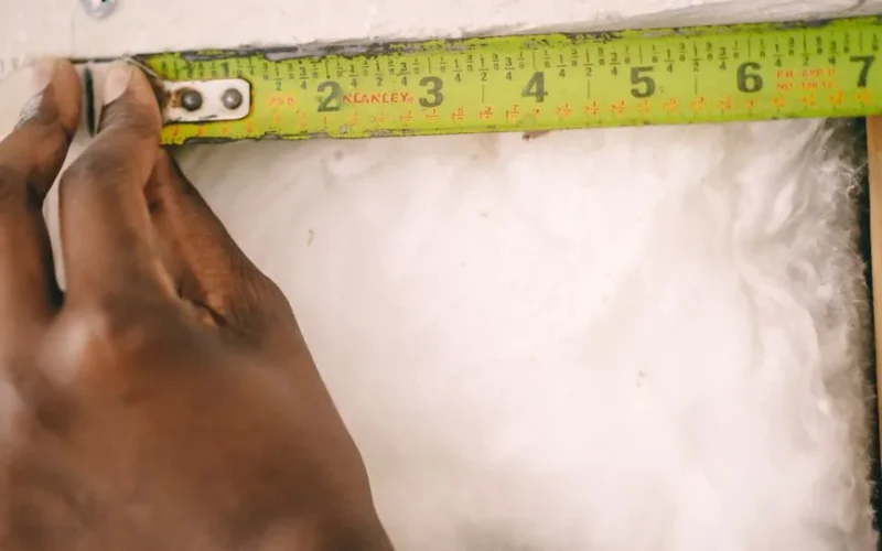 Close-up of a hand measuring insulation with a yellow tape measure.