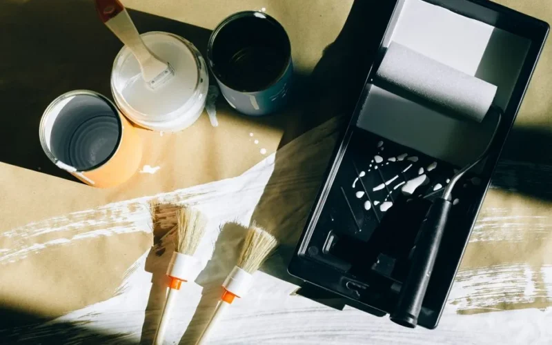 Top view of painting tools including brushes, rollers, and paint cans on paper.