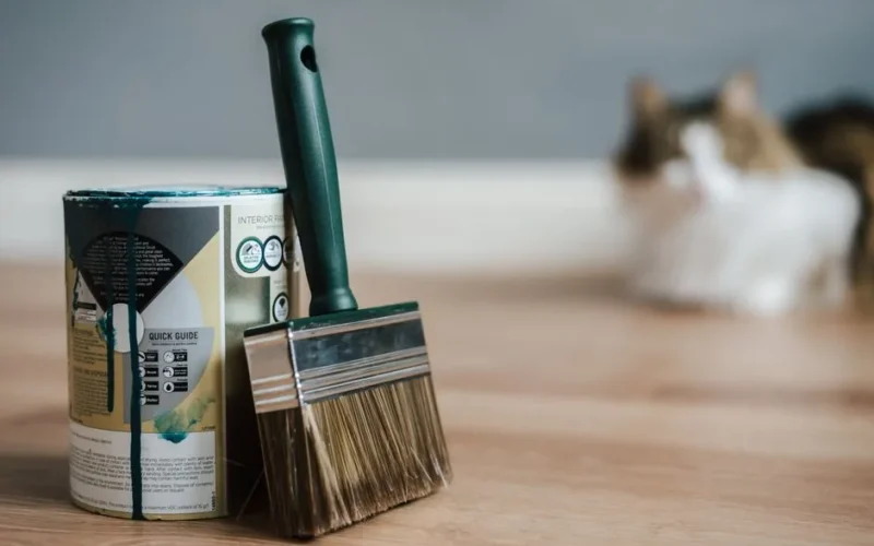 Professional paint brush near metal can with information and dirty flows on parquet in house