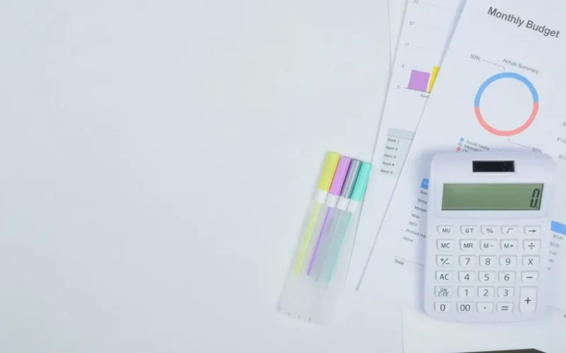 Minimalist office desk with a calculator, budget planning documents, and colorful pens.