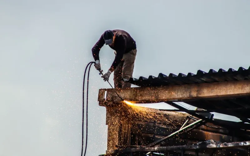 A worker cutting metal on a roof with visible sparks during construction work.