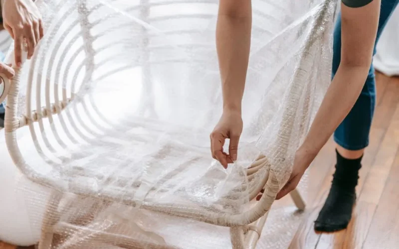 Close-up of a person wrapping a wooden chair in bubble wrap, preparing for moving or storage.
