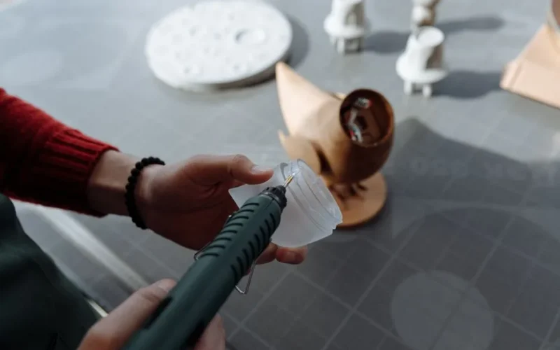 Close-up of hands using a glue gun in a workshop setting, crafting a wooden figurine.