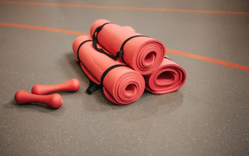 Red exercise mats and dumbbells on a gym floor, perfect for home or studio fitness.