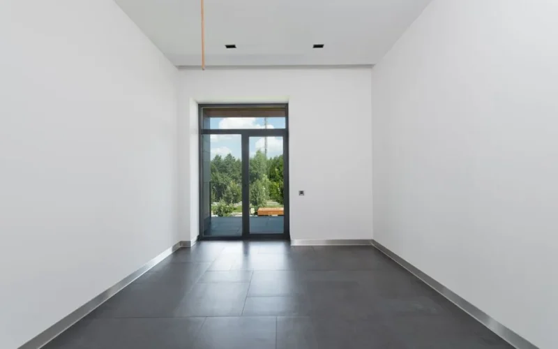 Interior of spacious room with tile flooring and white walls with glass doors in daylight