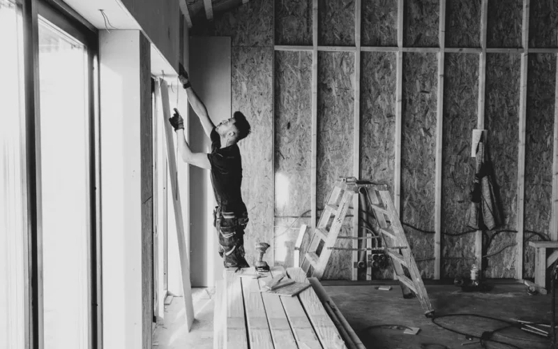 Black and white photo of a worker installing drywall indoors, Falun, Sweden.