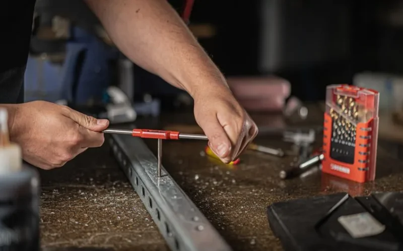 Close-up of hands using hand tools on metal in a workshop setting.